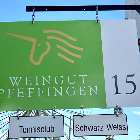 Ein Schild für das Weingut Pfeffingen mit der Hausnummer 15. Darunter befinden sich Schilder für einen Tennisclub und Schwarz Weiss.