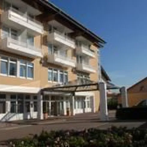 Ein modernes Gebäude mit mehreren Etagen und großen Fenstern. Die Fassade ist in warmen Farben gehalten und wirkt einladend.