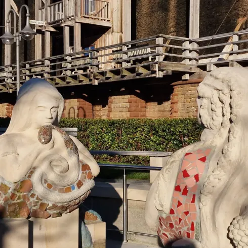 Zwei bemalte Skulpturen stehen sich gegenüber in einem modernen Außenbereich. Die eine Skulptur hat ein Meerestier und die andere eine detaillierte Frise aus Steinen und Mosaiken.