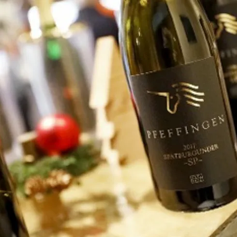 Eine Flasche Wein von Pfeffingen mit eleganter schwarzer Etikettierung. Im Hintergrund sind Weihnachtsdekorationen zu sehen.