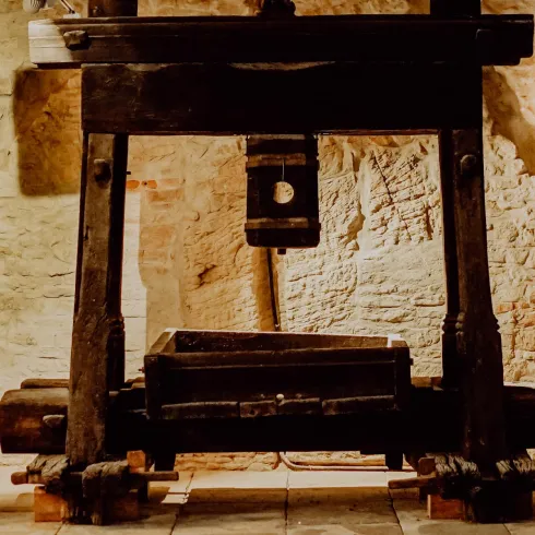 Ein historischer Weinkeller mit einer großen Holzpresse und Fässern. Die Wände sind mit kunstvollen Reliefs geschmückt.