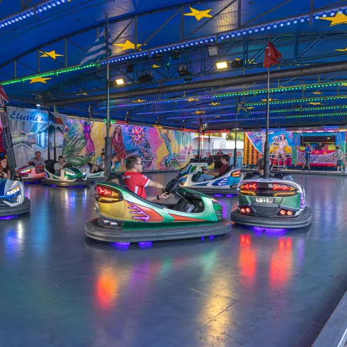 Ein Fahrgeschäft mit Autoscootern in einem bunten Indoor-Bereich. Die Dekoration und Lichter sorgen für eine lebhafte Atmosphäre.