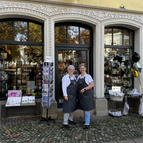 Ein charmantes Geschäft mit großen Fenstern und einem einladenden Eingang. Zwei Damen stehen freundlich vor dem Laden und lächeln in die Kamera.