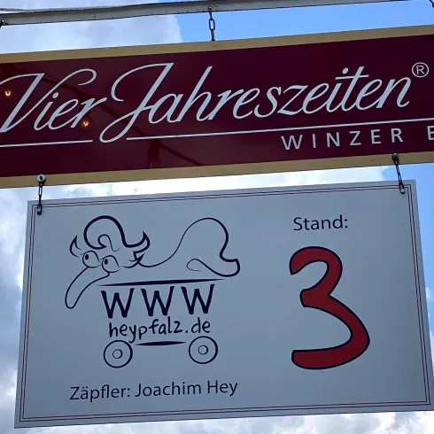 Ein hängendes Schild mit der Aufschrift "Vier Jahreszeiten Winzer EG" und der Standnummer 3. Darunter steht die Website www.heypfalz.de und der Name des Zapfler, Joachim Hey.