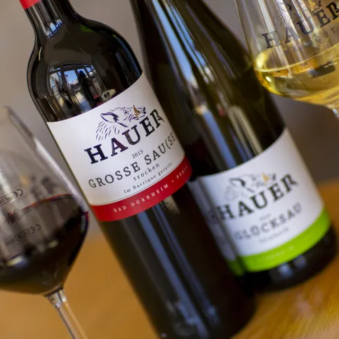 Ein attraktives Arrangement von Weinen auf einem Holzuntergrund. Zu sehen sind eine Flasche Rotwein, eine Flasche Weißwein und ein Glas mit Rotwein.