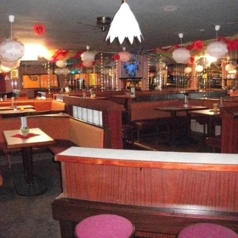 Ein gemütliches Restaurant mit bunten Lampen und Holzinterieur. Die Tische sind ordentlich eingedeckt und die Atmosphäre wirkt einladend.