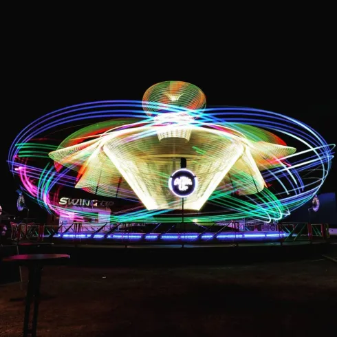 Ein leuchtender Fahrgeschäft mit bunten Lichtern dreht sich im Dunkeln. Die leuchtenden Farben erzeugen eine lebhafte Atmosphäre.
