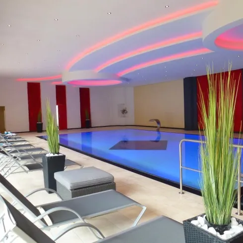 Ein eleganter Innenpool mit bequemen Liegen und stilvollen Pflanzen. Die Beleuchtung schafft eine entspannte Atmosphäre.