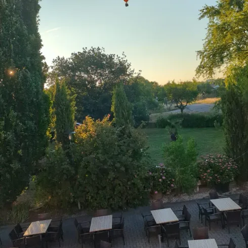 Ein Heißluftballon schwebt über einem grünen Garten. Darunter stehen Tische und Stühle in einem gemütlichen Außenbereich.