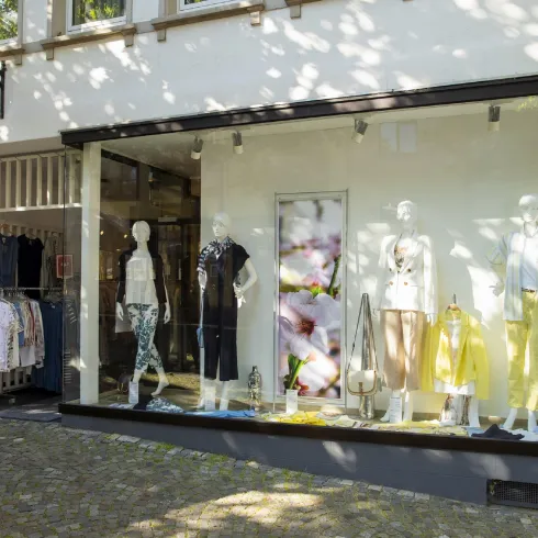 Ein modernes Schaufenster mit mehreren Schaufensterpuppen, die verschiedene Kleidungsstücke präsentieren. Die Atmosphäre ist hell und einladend, ideal für modebewusste Kunden.