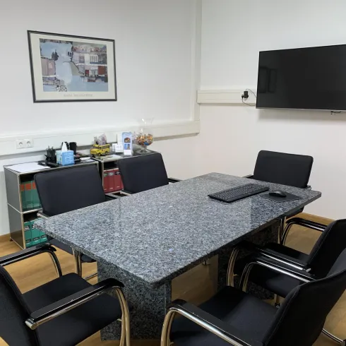 Ein modernes Besprechungszimmer mit einem Granittisch und schwarzen Stühlen. An der Wand hängt ein Fernseher und ein Bild.