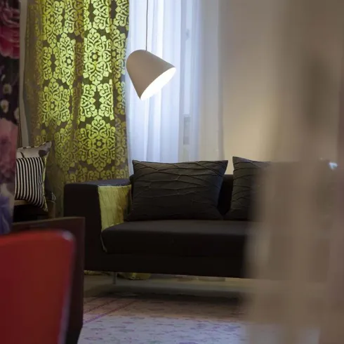 Ein stilvoller Wohnraum mit einem dunklen Sofa und bunten Vorhängen. Ein Stehlampe sorgt für angenehmes Licht.