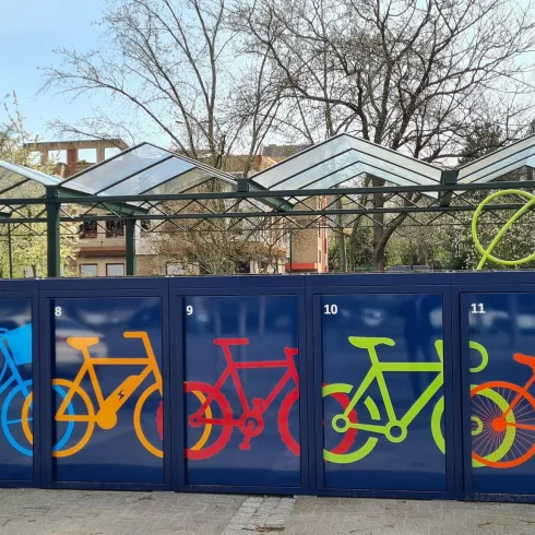 Eine Fahrradstation mit bunten Fahrradillustrationen auf blauen Wänden. Im Hintergrund sind transparenten Dächer zu sehen.
