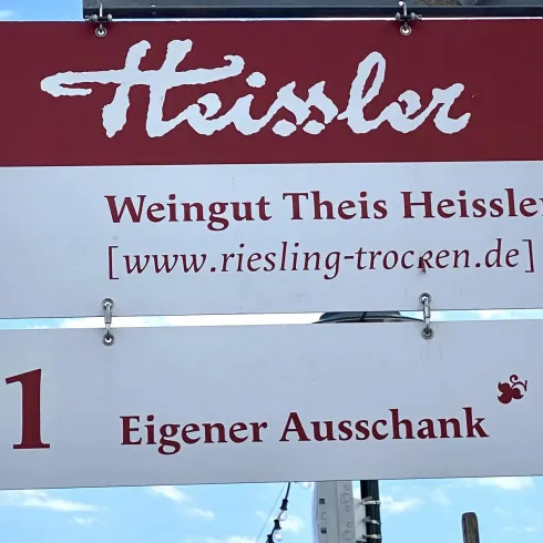 Ein Hinweisschild für das Weingut Theis Heissler. Es zeigt die Hausnummer 11 und die Webseite www.riesling-trocken.de.