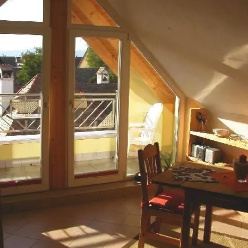 Ein gemütlicher Raum im Dachgeschoss mit großen Fenstern und einem Tisch. Das Licht fällt sanft in den Raum und schafft eine einladende Atmosphäre.