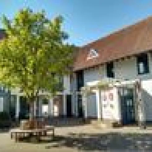 Ein modernes Gebäude mit einem großen Baum im Innenhof. Der Himmel ist klar und sonnig.