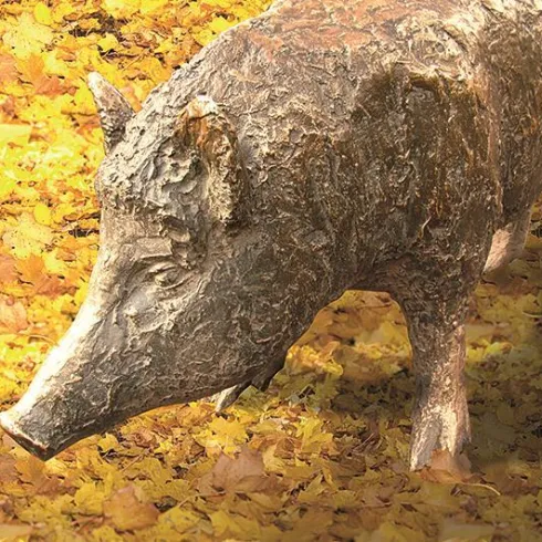 Eine Statue eines Wildschweins, kunstvoll aus Holz geschnitzt. Umgeben von bunten Herbstblättern.