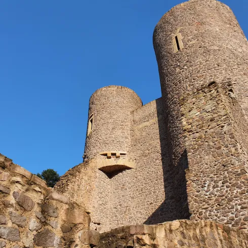 Eine alte Burg mit zwei Türmen und einem klaren blauen Himmel. Die Steinmauern sind gut erhalten und zeigen die historische Architektur.