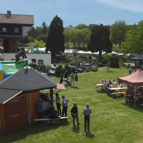 Eine Veranstaltung im Freien mit vielen Menschen auf einer Wiese. Es gibt Essensstände, eine Sprungburg und ein schönes Wetter.