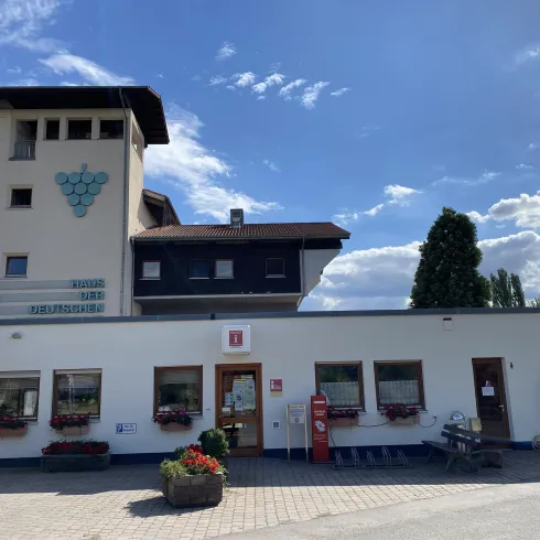 Ein modernes Gebäude mit einem Turm und einer einladenden Fassade. Es gibt Fenster mit Blumenkästen und einen klaren blauen Himmel.