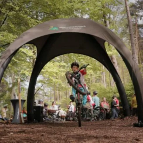 <p>Halbrunder offener Bogen, darunter ein Kind auf dem Fahrrad. Das Kind mit Schutzkleidung und Helm balanciert auf dem Hinterreifen