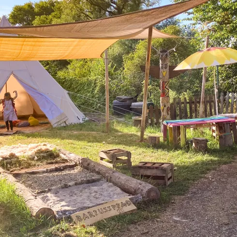 Ein Campingplatz mit einem detaillierten Lageplan und verschiedenen Stellplätzen. Im Vordergrund ist eine Familie vor einem Zelt zu sehen, die die Natur genießt.
