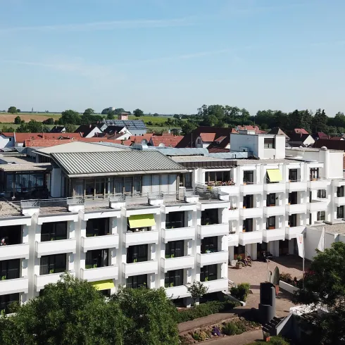 Ein modernes Gebäude mit mehreren Etagen und großen Fenstern. Umgeben von Bäumen und Wohngebieten, strahlt es eine einladende Atmosphäre aus.