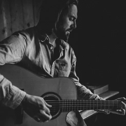 Ein Mann spielt Gitarre in einem dunklen Raum. Die Atmosphäre ist ruhig und nachdenklich.