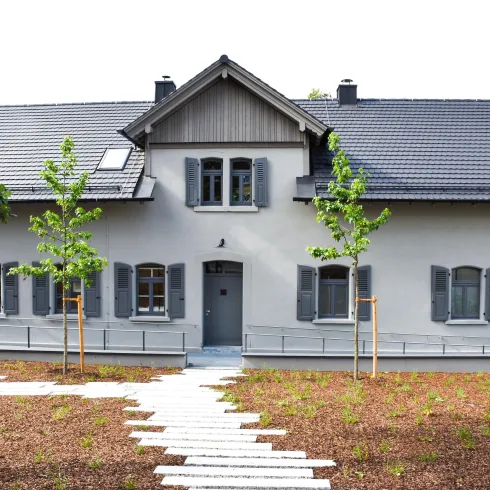 Ein modernes Haus mit grauen Fensterläden und einem schlichten Design. Der Garten ist gepflegt und enthält einige junge Bäume.
