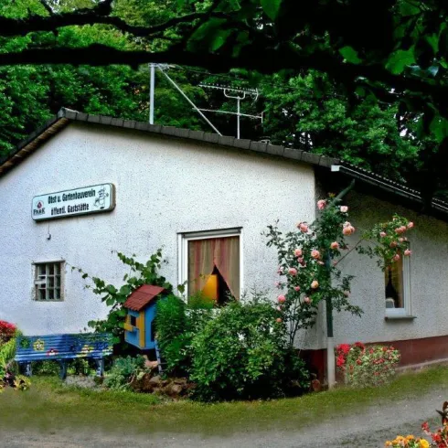 Ein gemütliches Haus im Grünen mit blühenden Pflanzen und einem kleinen Spielhaus. Der Eingang ist einladend und von einer bunten Gartenlandschaft umgeben.