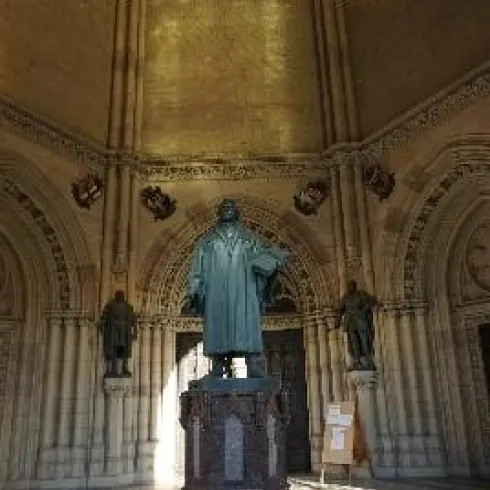 Eine Statue von Martin Luther steht im Zentrum eines gotischen Raumes. Helle Lichtstrahlen fallen durch die Fenster und schaffen eine beeindruckende Atmosphäre.