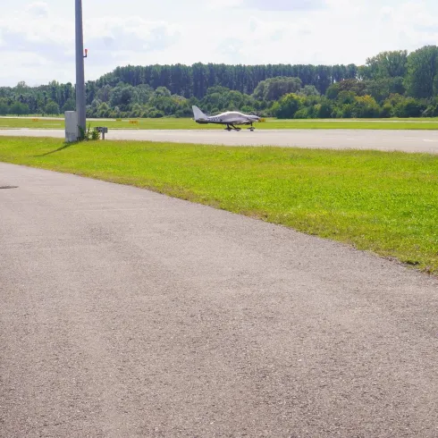Ein kleiner Flugzeug rollt auf einem Flughafen. Neben der Startbahn verläuft ein gepflasterter Weg.
