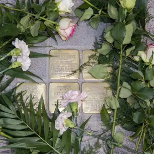 Eine Gedenkstätte mit mehreren Messingtafeln, umgeben von frischen Blumen. Die Blumen symbolisieren Erinnerung und Ehrfurcht.