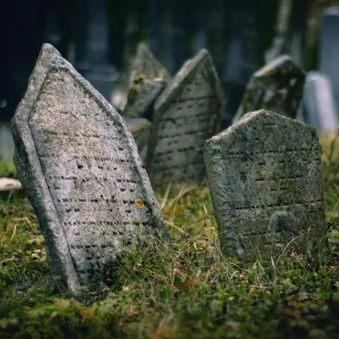 Ein alter Friedhof mit schiefen Grabsteinen, umgeben von Gras. Die Atmosphäre wirkt ruhig und melancholisch.