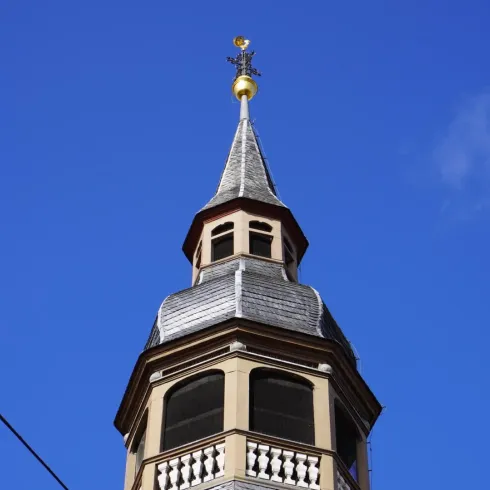 Ein schmaler Kirchturm mit einem eleganten Spitzdach. Der Himmel ist klar und blau.