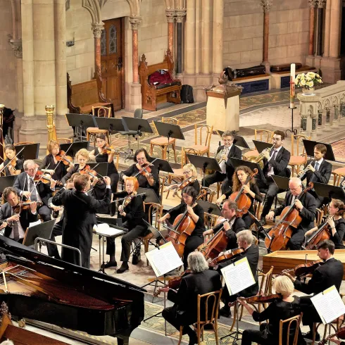 Ein Orchester spielt in einer Kirche. Die Musiker sind konzentriert und es herrscht eine festliche Atmosphäre.