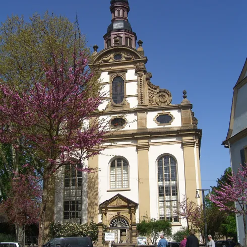 Eine beeindruckende Kirche mit einer markanten Architektur. Vor der Kirche blühen rosa Bäume und Menschen schlendern auf dem Platz.