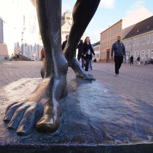 Eine Statue von Füßen steht auf einem Pflastersteinboden. Menschen gehen im Hintergrund vorbei.