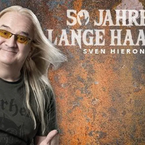 Ein lächelnder Mann mit langen, blonden Haaren trägt ein schwarzes T-Shirt. Im Hintergrund steht der Schriftzug „50 Jahre lange Haare“.