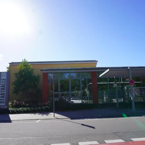 Ein modernes Gebäude mit großen Fenstern und kräftigen Farben. Im Hintergrund sind Bäume und ein klarer blauer Himmel sichtbar.