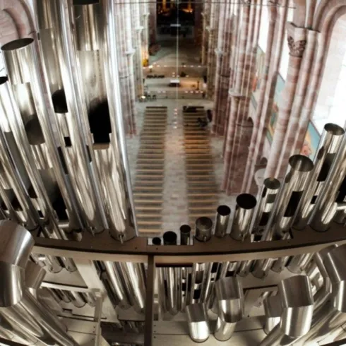 Eine beeindruckende Orgel mit vielen metallischen Pfeifen ist im Vordergrund zu sehen. Im Hintergrund erstreckt sich der große Raum einer Kirche.