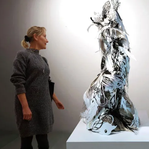 Eine Frau betrachtet eine filigrane Skulptur aus Papier. Die Skulptur hat eine komplexe Form und schimmert in Weiß und Schwarz.