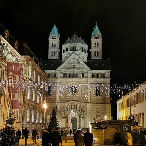 Ein historisches Gebäude bei Nacht, beleuchtet von Lichtern. Menschen spazieren auf der Straße, umgeben von festlicher Dekoration.