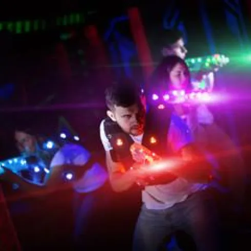 Eine Gruppe von Menschen spielt Laser Tag in einer bunten, beleuchteten Umgebung. Die Teilnehmer tragen spezielle Westen und halten Laser-Pistolen.