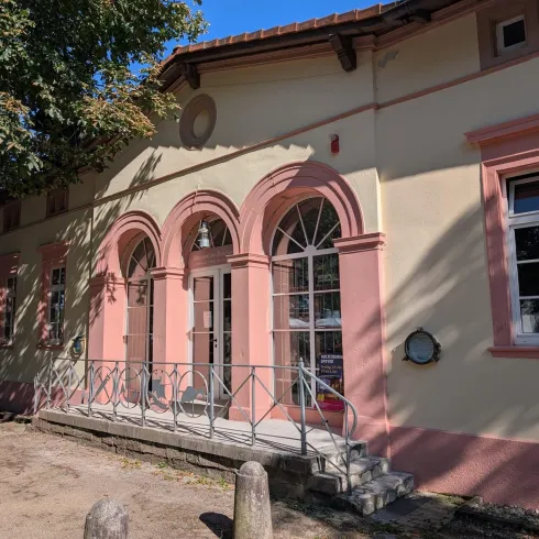 Ein historisches Gebäude mit einer schönen Fassade in sanften Farben. Die große Fensterfront und der Balkon verleihen dem Bauwerk eine einladende Note.