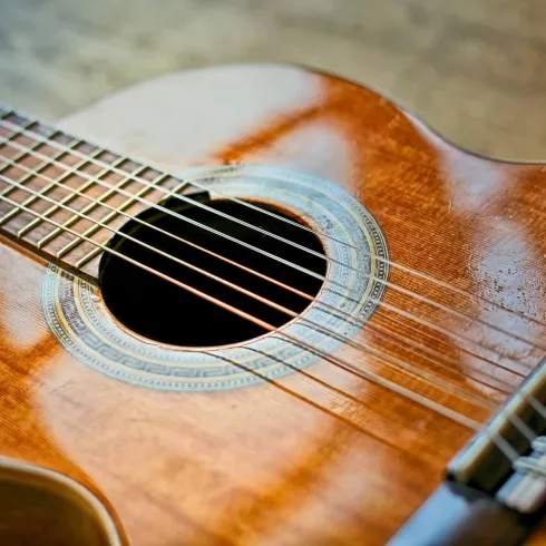 Eine akustische Gitarre mit einem glänzenden Holzfinish. Die Saiten sind sichtbar und der Klangkörper hat eine schöne runde Form.