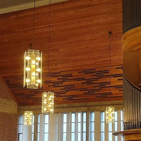 Ein moderner Innenraum mit einer beeindruckenden Holzdecke und einer spiralförmigen Treppe. Leuchtende Pendelleuchten ergänzen das elegante Design.