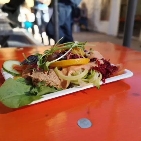 Ein Teller mit frischem Salat, der auf einem orangefarbenen Tisch steht. Der Salat enthält verschiedene Gemüsesorten und ist mit Kräutern garniert.