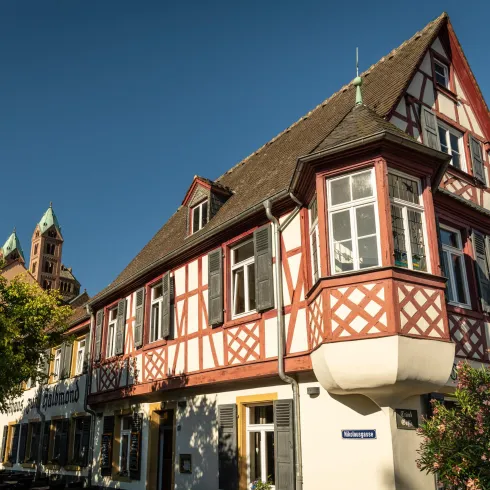 Ein charmantes Gebäude mit Fachwerkstil und bunten Fensterrahmen. Im Hintergrund ist ein Kirchturm sichtbar und der Himmel ist klar.
