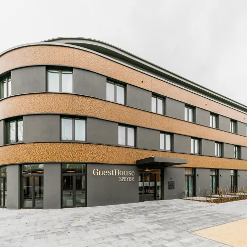 Ein modernes Gästehaus mit einer auffälligen Fassade aus Holz und Beton. Das Gebäude hat große Fenster und einen einladenden Eingangsbereich.
